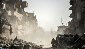 (FILES) This file photo taken on October 20, 2017 shows fighters of the Syrian Democratic Forces (SDF) walking down a street in Raqa past destroyed vehicles and heavily damaged buildings after a Kurdish-led force expelled Islamic State (IS) group fighters from the northern Syrian city, formerly their "capital". 2017 will be remembered as the year the Islamic State organisation's ultra-violent experiment in statehood was terminated but Iraq and Syria are left staring at ruined cities and daunting challenges. / AFP / BULENT KILIC