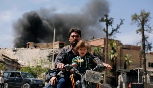 A man and a boy ride a motorbike at the city of Douma in Damascus