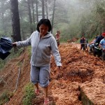 A resident walks on the side of a road as police officers and fire marshals clear debris and fallen trees caused by a landslide at the height of Typhoon Mangkhut that hit Bokod, Benguet