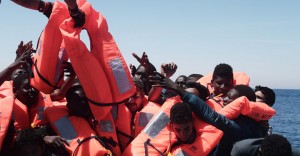 Migrants in an overcrowded plastic raft reach out for life jackets during a search and rescue operation by rescue ship Aquarius, operated by SOS Mediterranean and Doctors without Borders