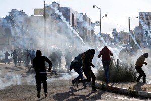 Palestinian protesters run from tear gas fired by Israeli troops during clashes at a protest against U.S. President Donald Trump's decision to recognize Jerusalem as the capital of Israel, near the Jewish settlement of Beit El, near Ramallah